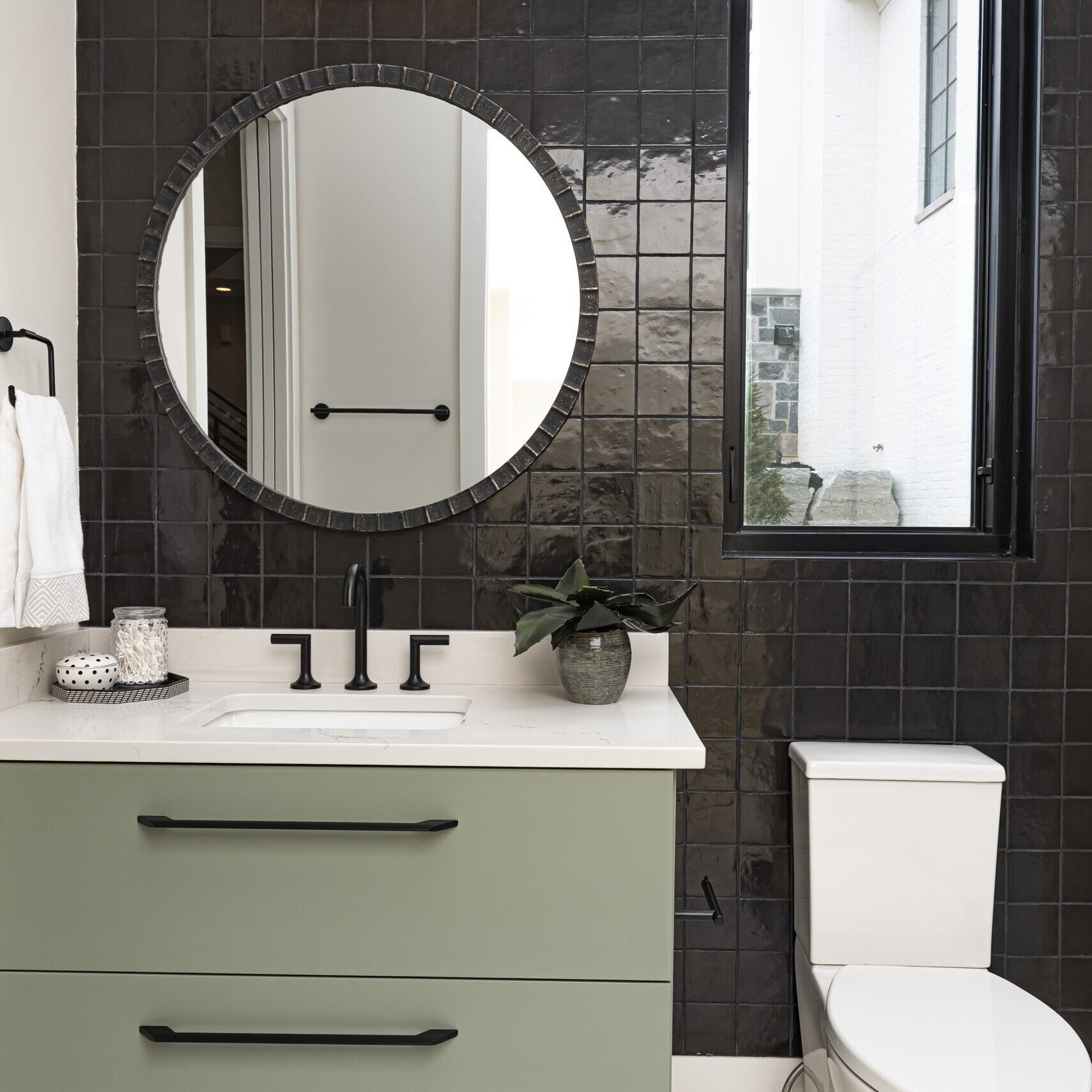 A bathroom with black and white tile and a round mirror.