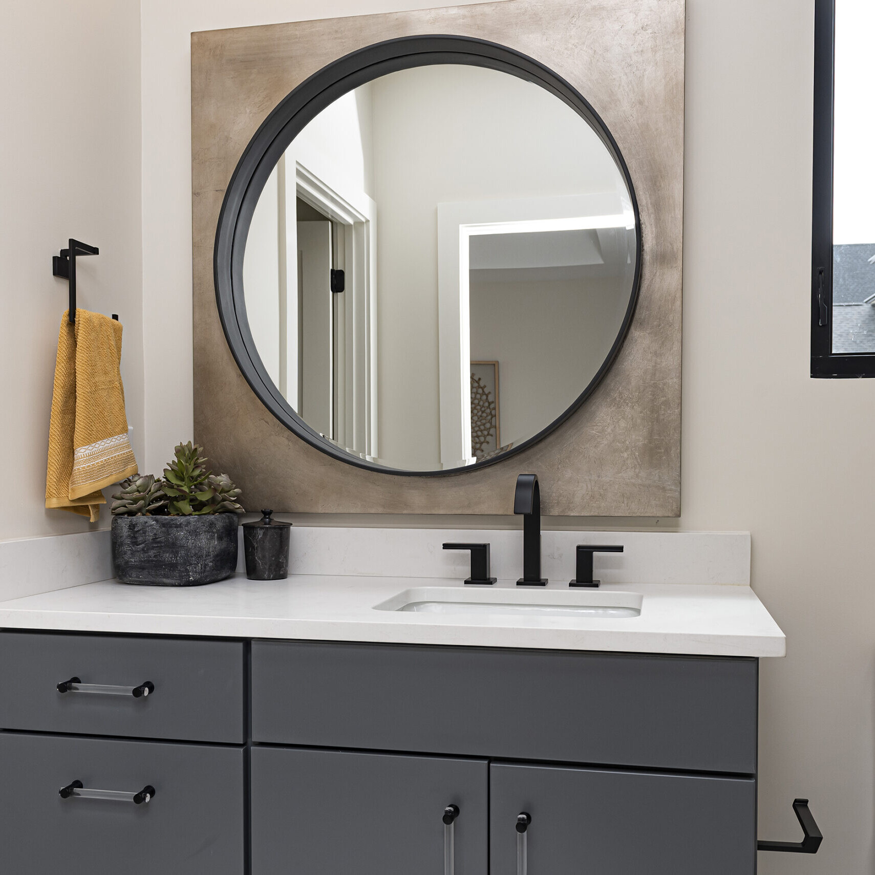 A bathroom with a grey vanity and a round mirror.