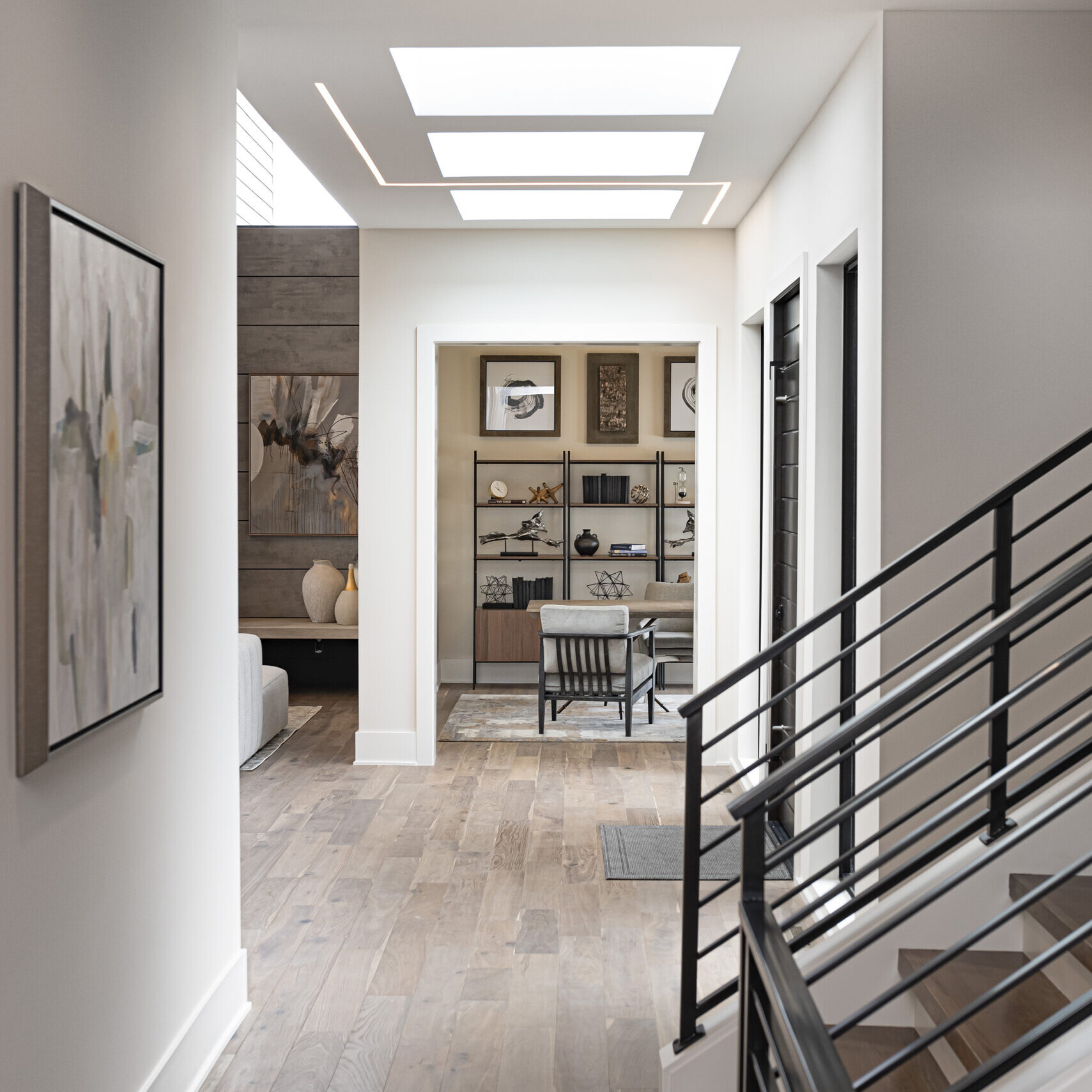 A hallway in a modern home with wood flooring and a light fixture.