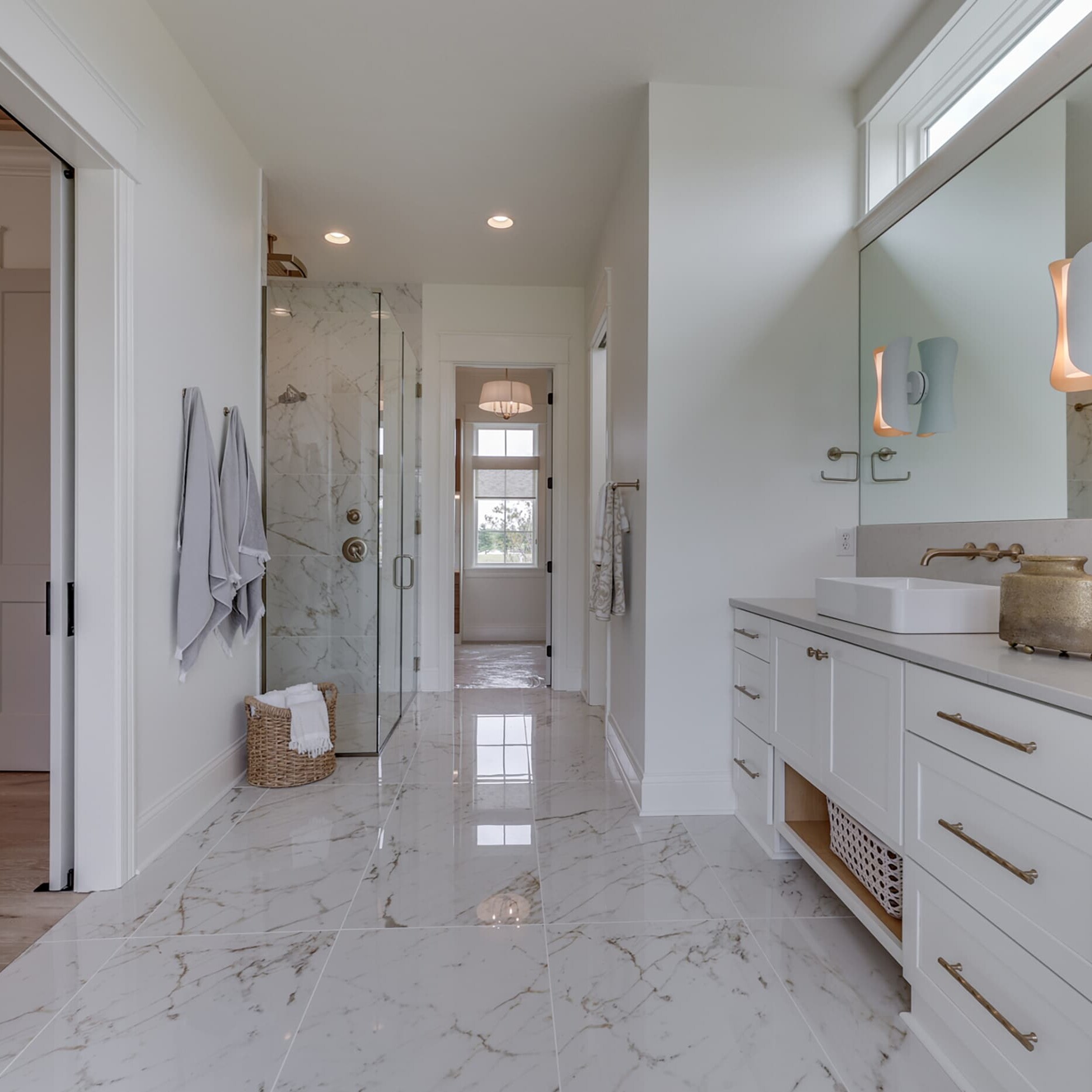 A white bathroom with marble counter tops and a glass shower.