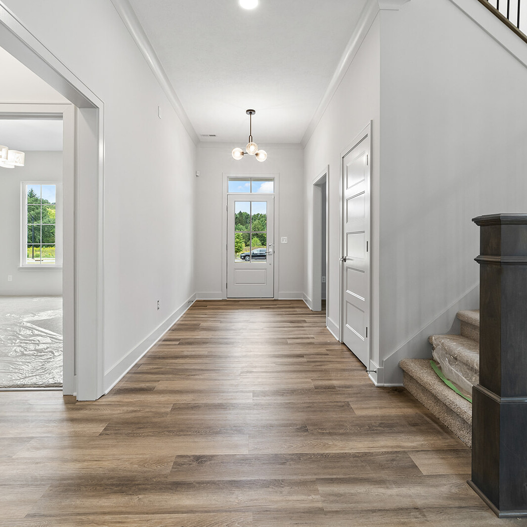 A custom home hallway in Indianapolis adorned with hardwood floors and a grand staircase.