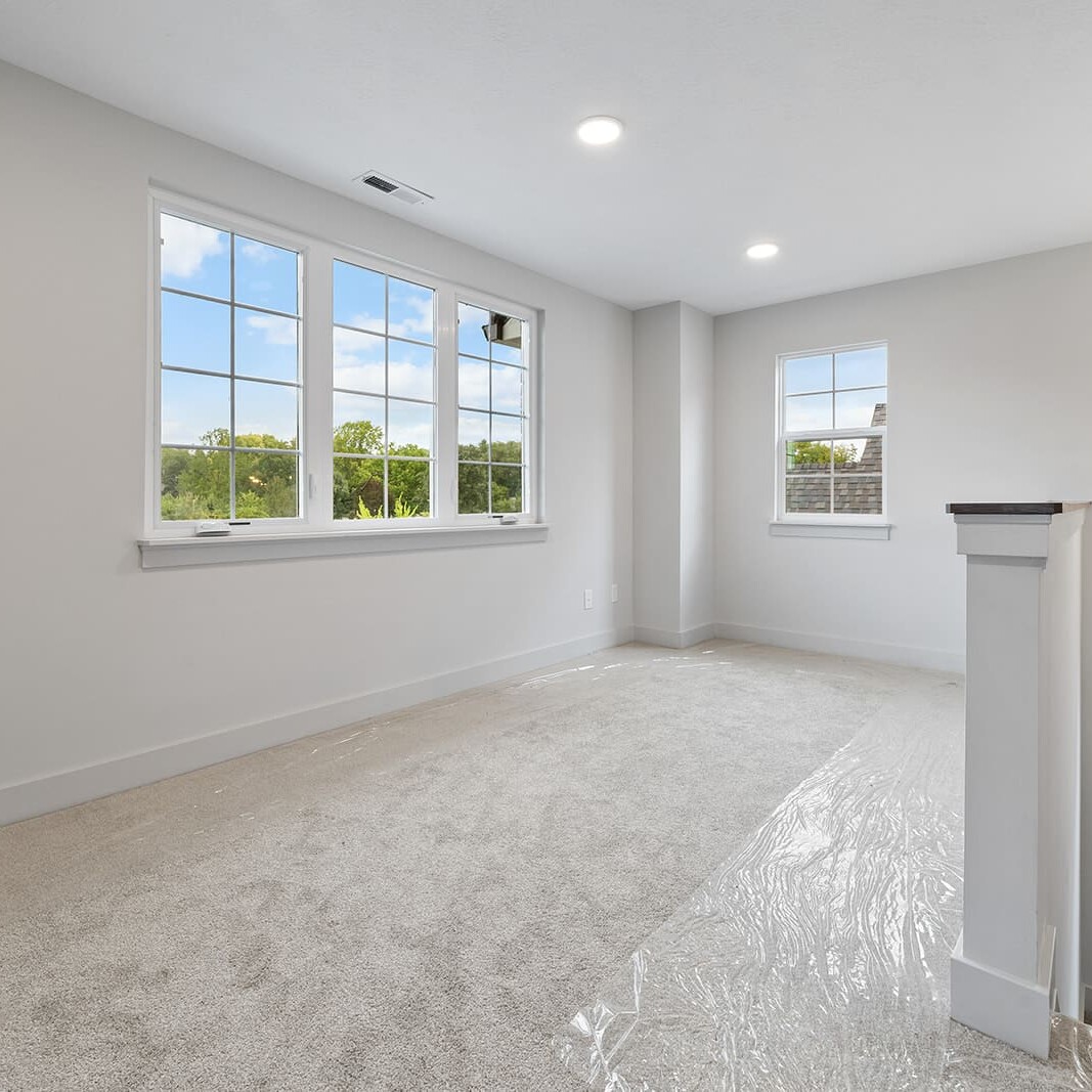 An empty room with white carpet and windows, designed by a luxury custom home builder in Westfield Indiana.