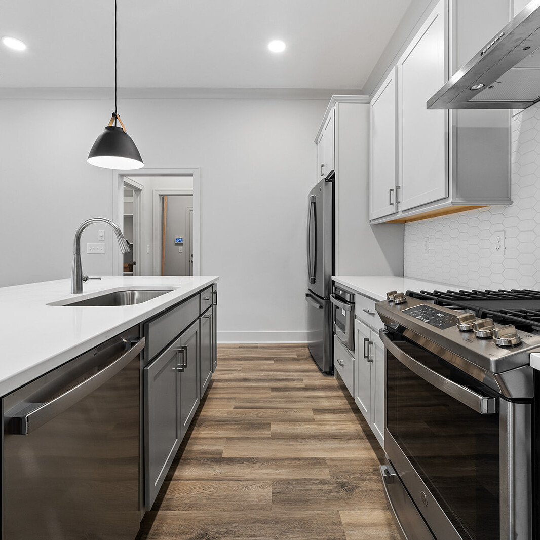 A white kitchen with stainless steel appliances and wood floors in a luxury custom home.