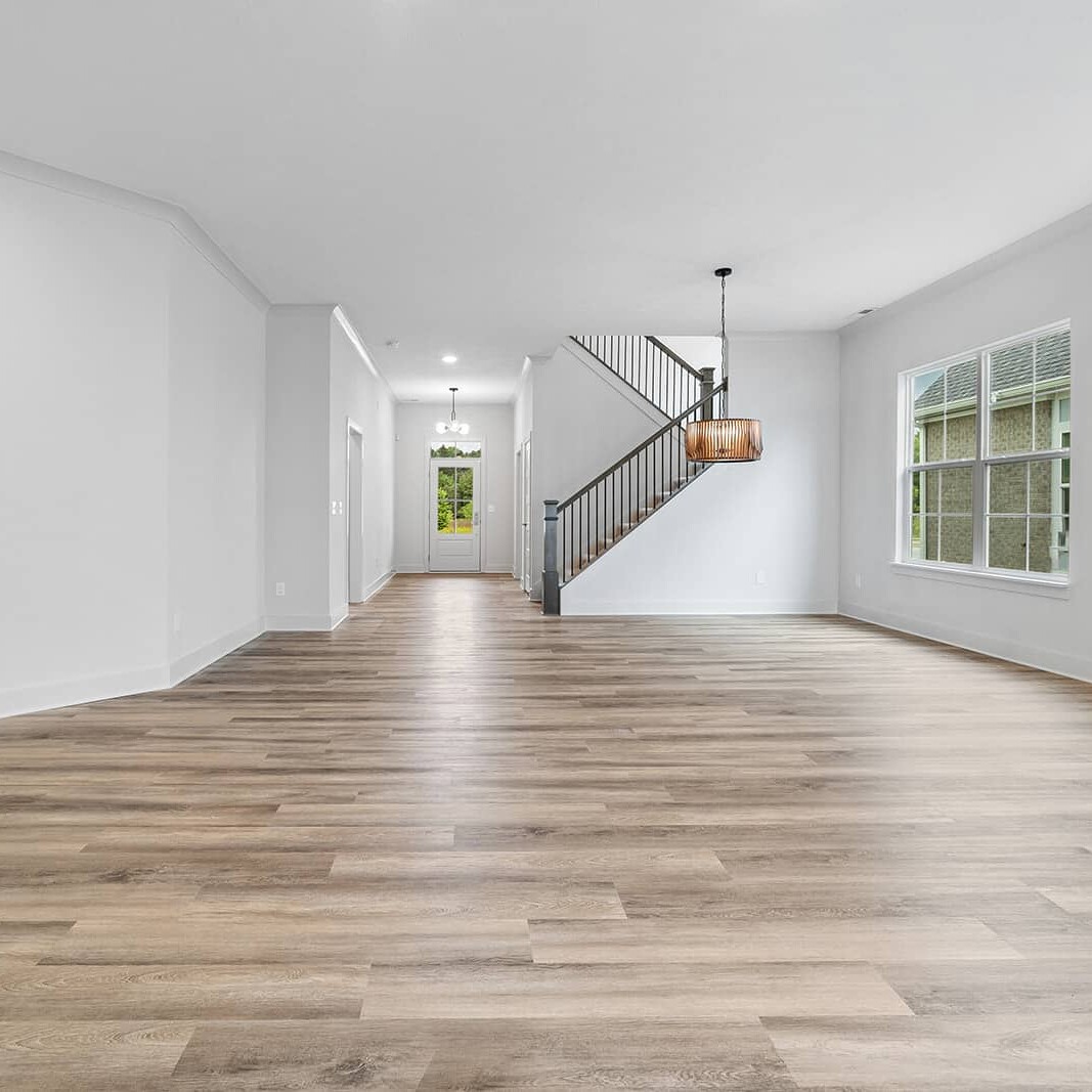 An empty living room with wood floors and white walls in a custom home.