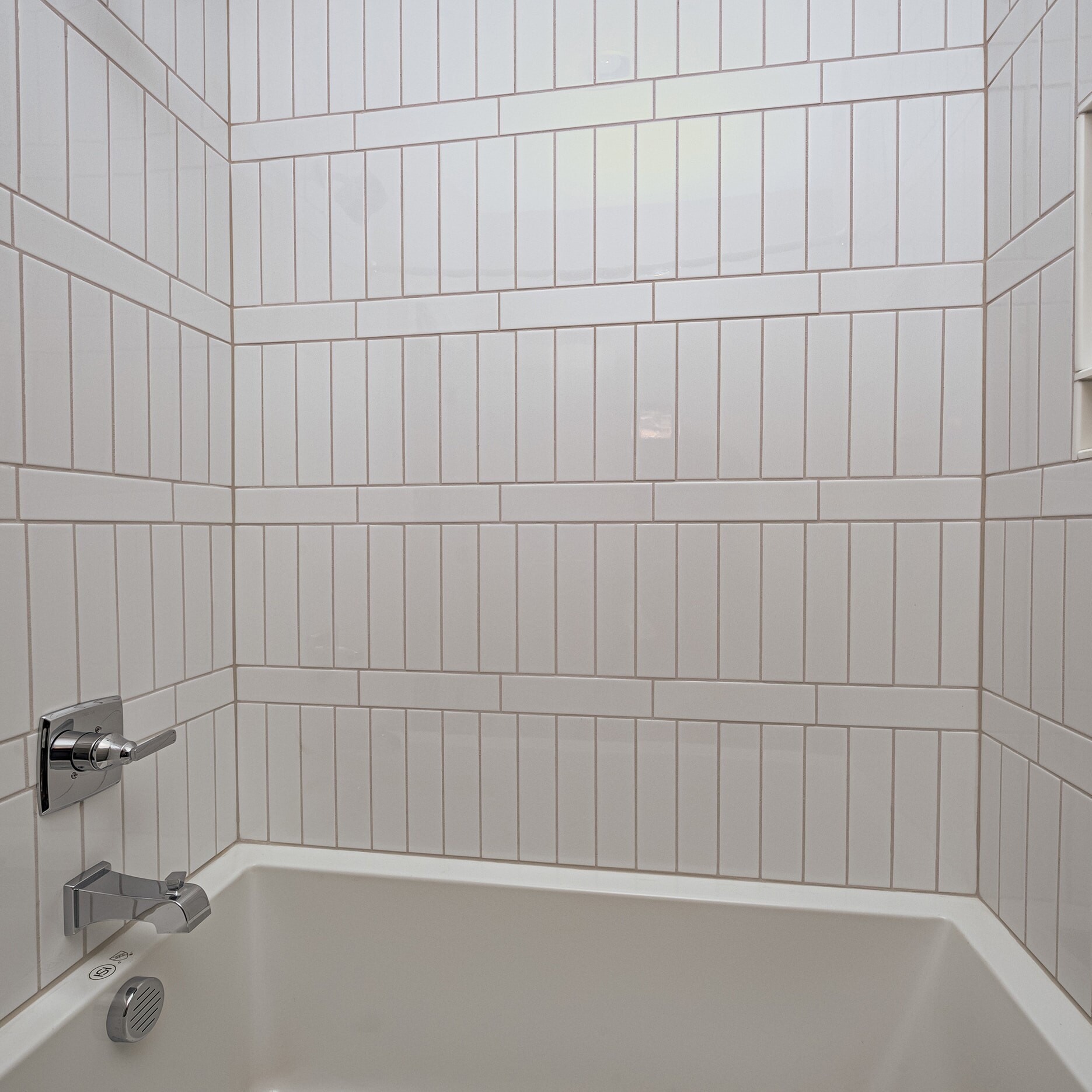 A white tiled bathroom with a tub.
