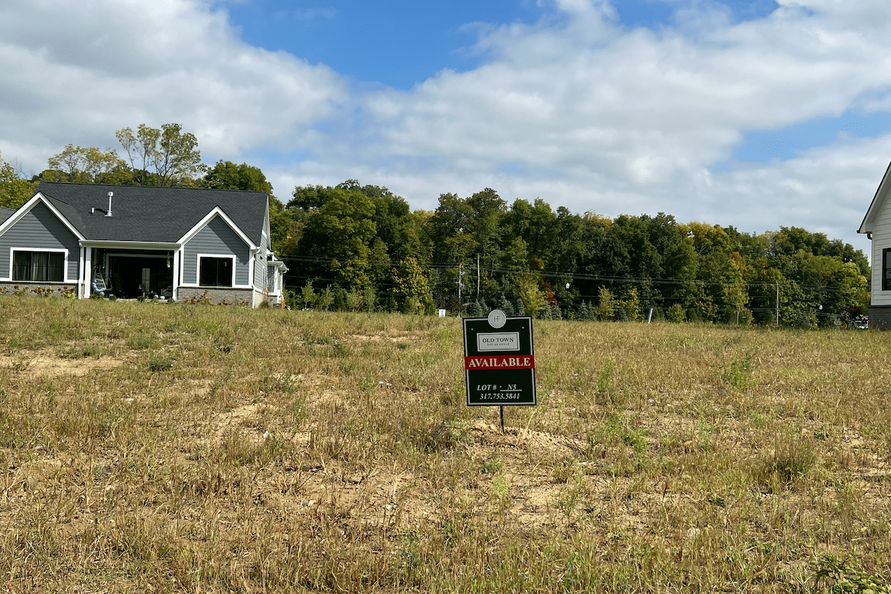 Two houses in the middle of a field with a for sale sign, built by a luxury custom home builder in Westfield Indiana.