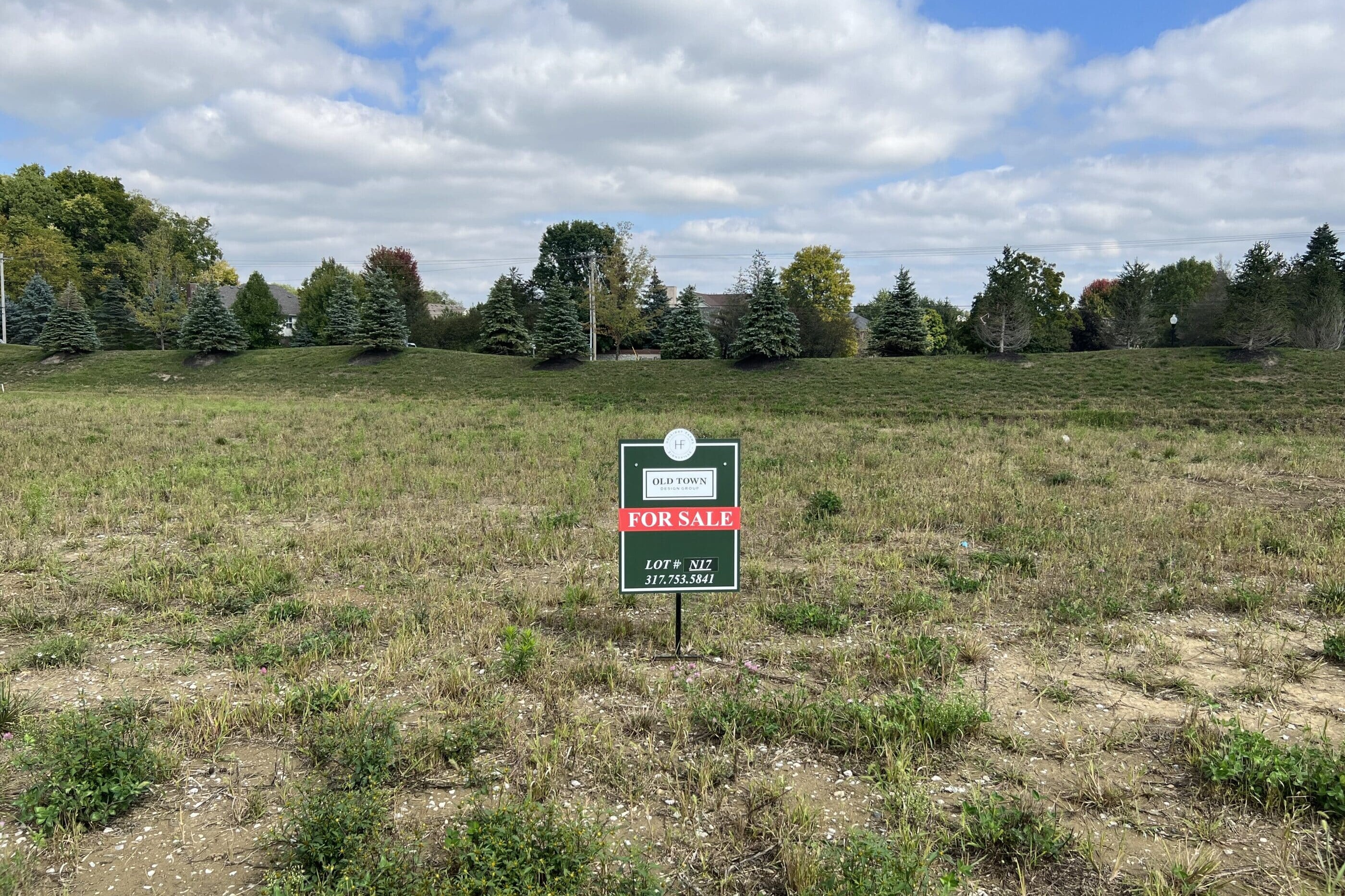 A vacant lot with a sign in the middle of a field. Featuring new homes for sale in Carmel Indiana.