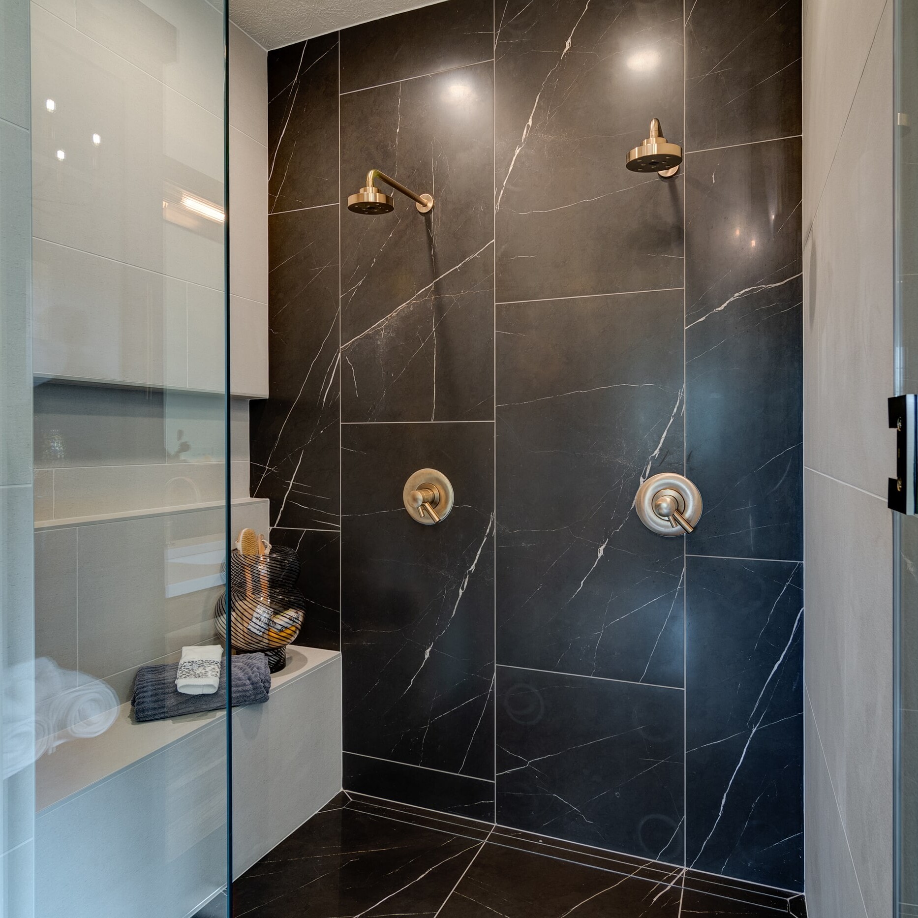 A bathroom with a glass shower door and black tile.