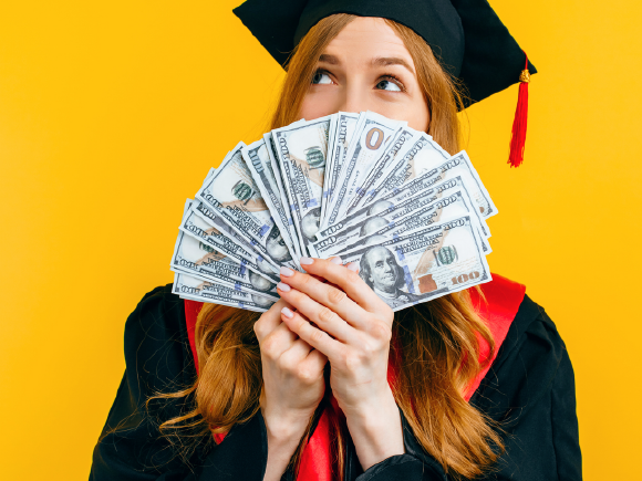 A woman in a graduation cap and gown showcasing her future career opportunities with money in her hands.